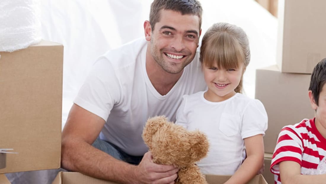 Father and daughter holding a teddy bear among packed moving boxes